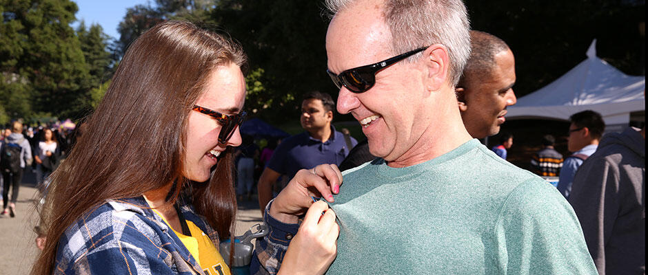 young woman pins something on shirt of older man outside